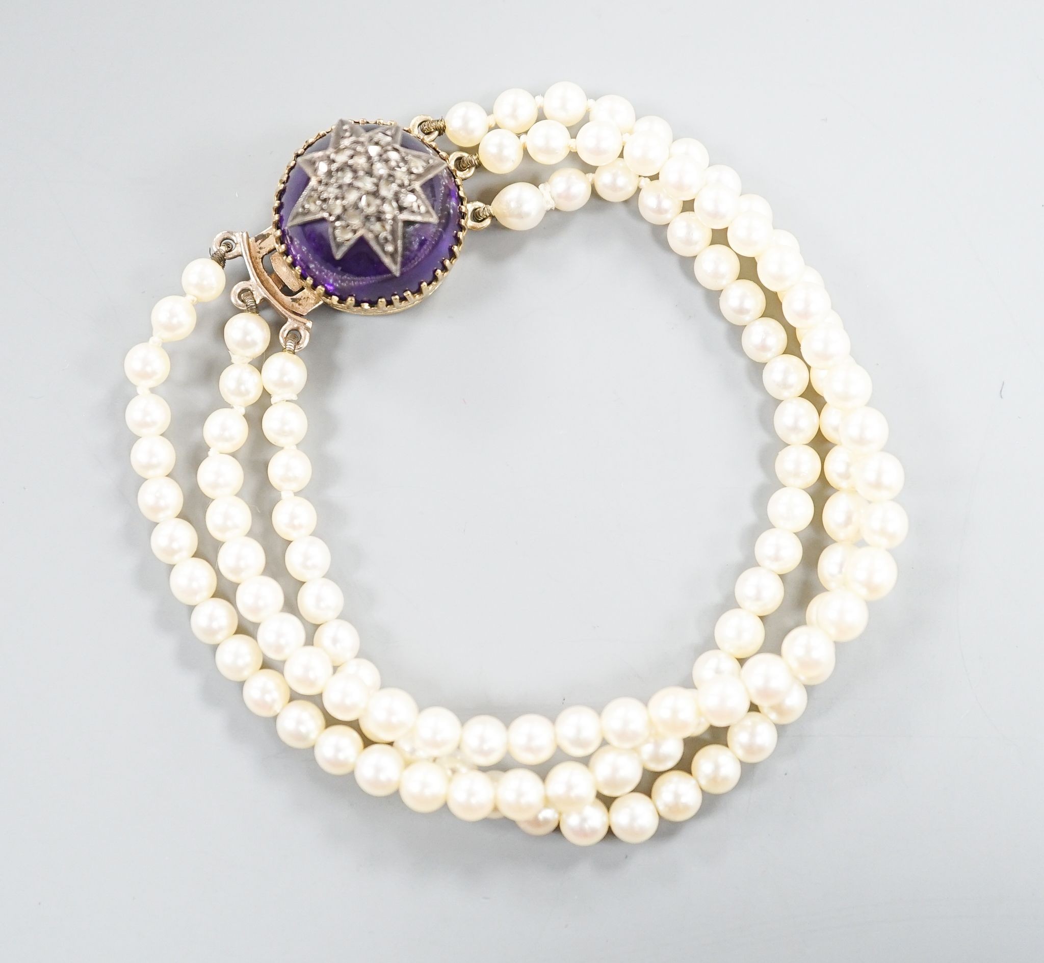 An early 20th century triple strand cultured? pearl bracelet, with rose cut diamond and cabochon amethyst set yellow metal clasp, 17.5cm, gross weight 21 grams.